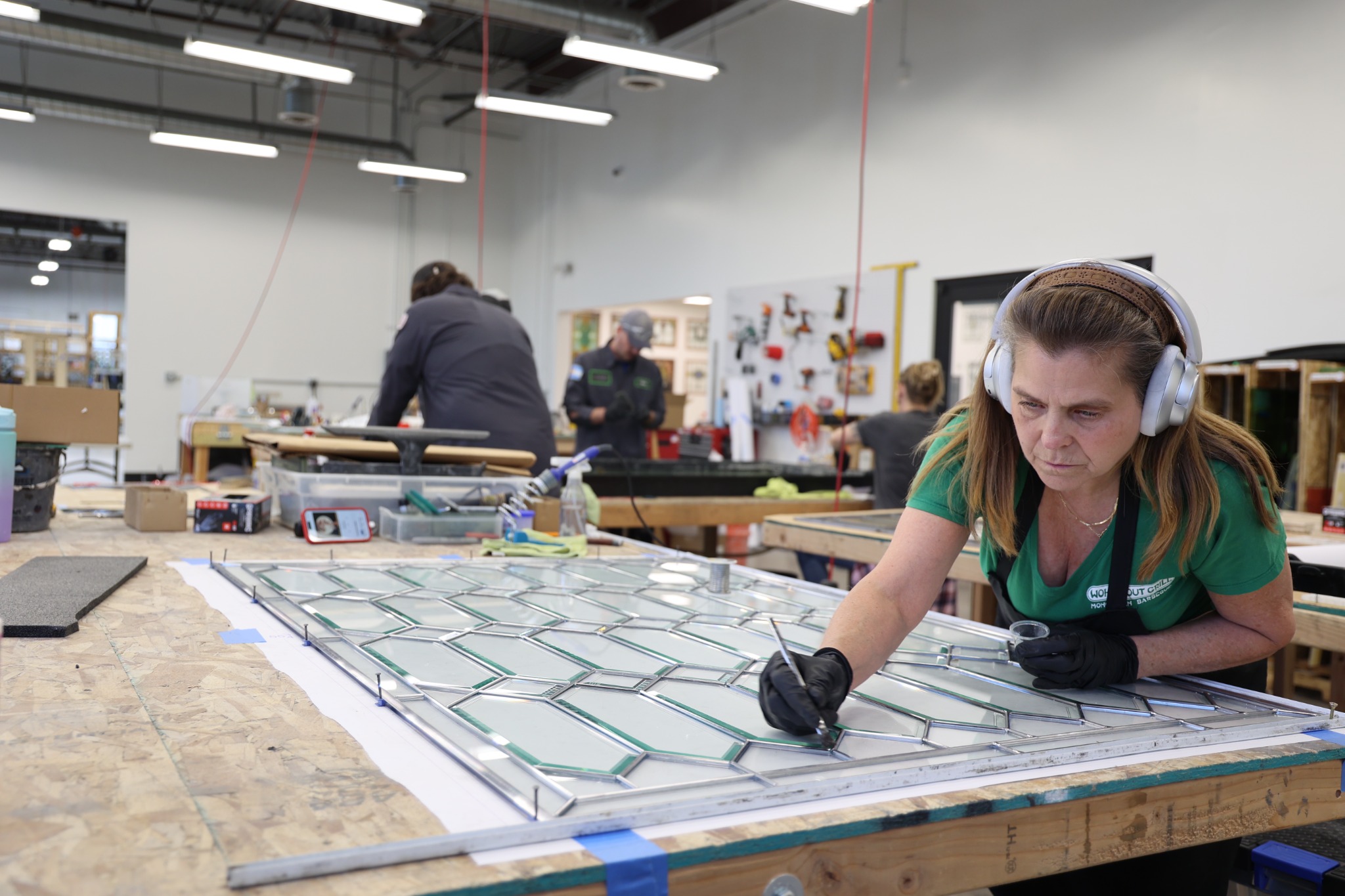 Scottish Stained Glass craftsperson working carefully across a large leaded glass panel at the workshop table.