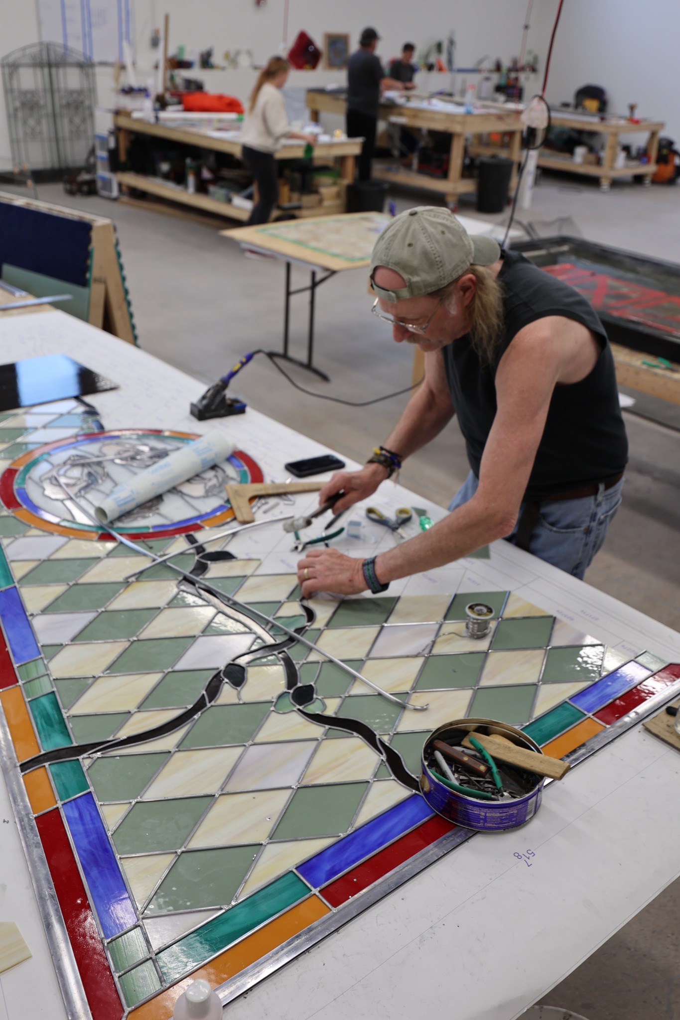 Scottish Stained Glass craftsperson assembling a large leaded glass panel at a workshop table.